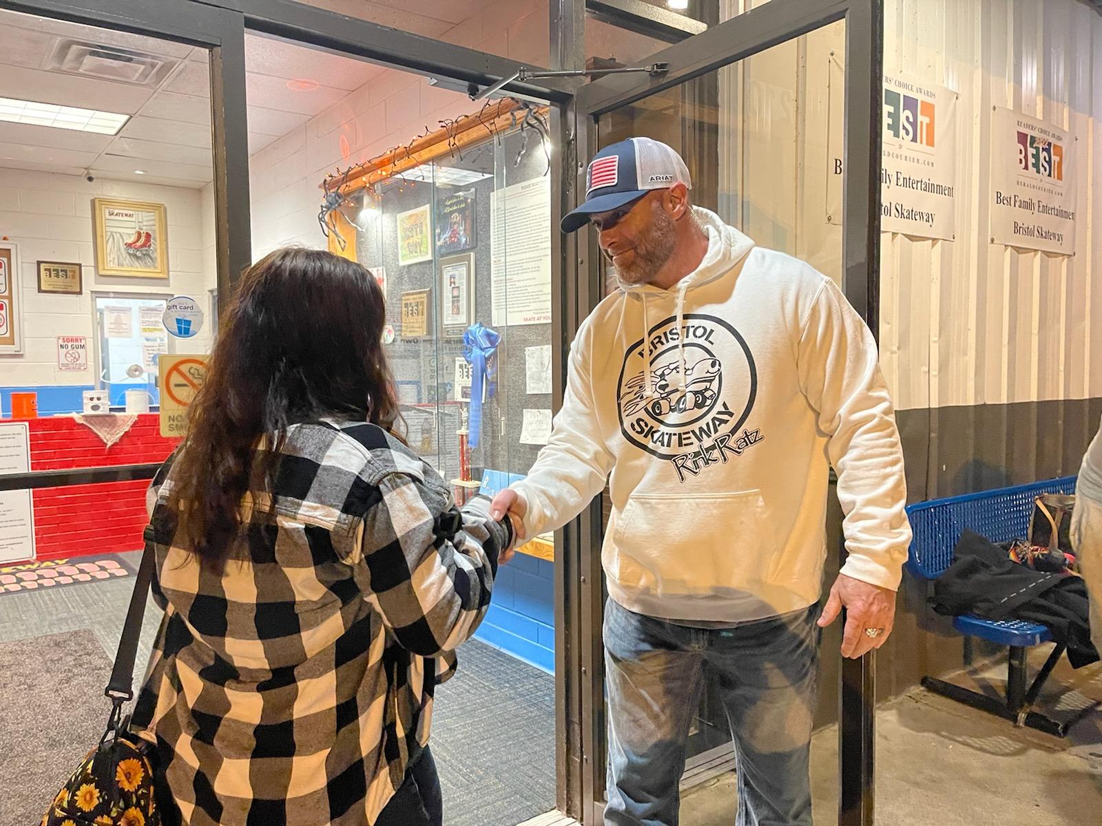 Teen in a plaid jacket being greeted by a man in a hooded sweatshirt outside a roller skating rink